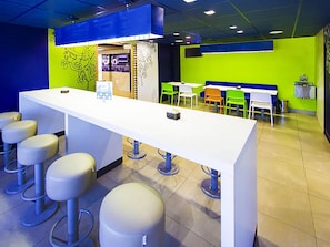 A modern bar area with a white counter, stools, and a seating area with chairs. - ibis budget Sertaozinho (Sertaozinho)