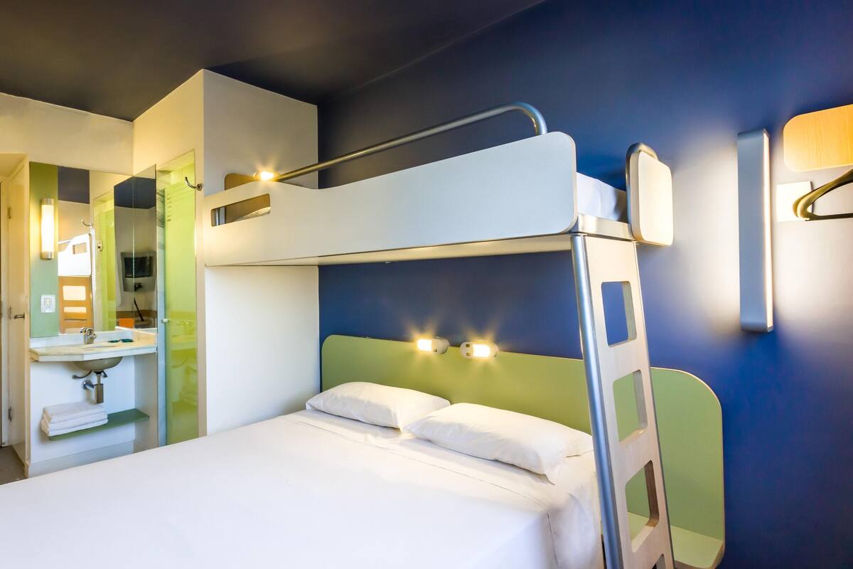 Una cama litera con cabecera, una mesita de noche y un espejo.
