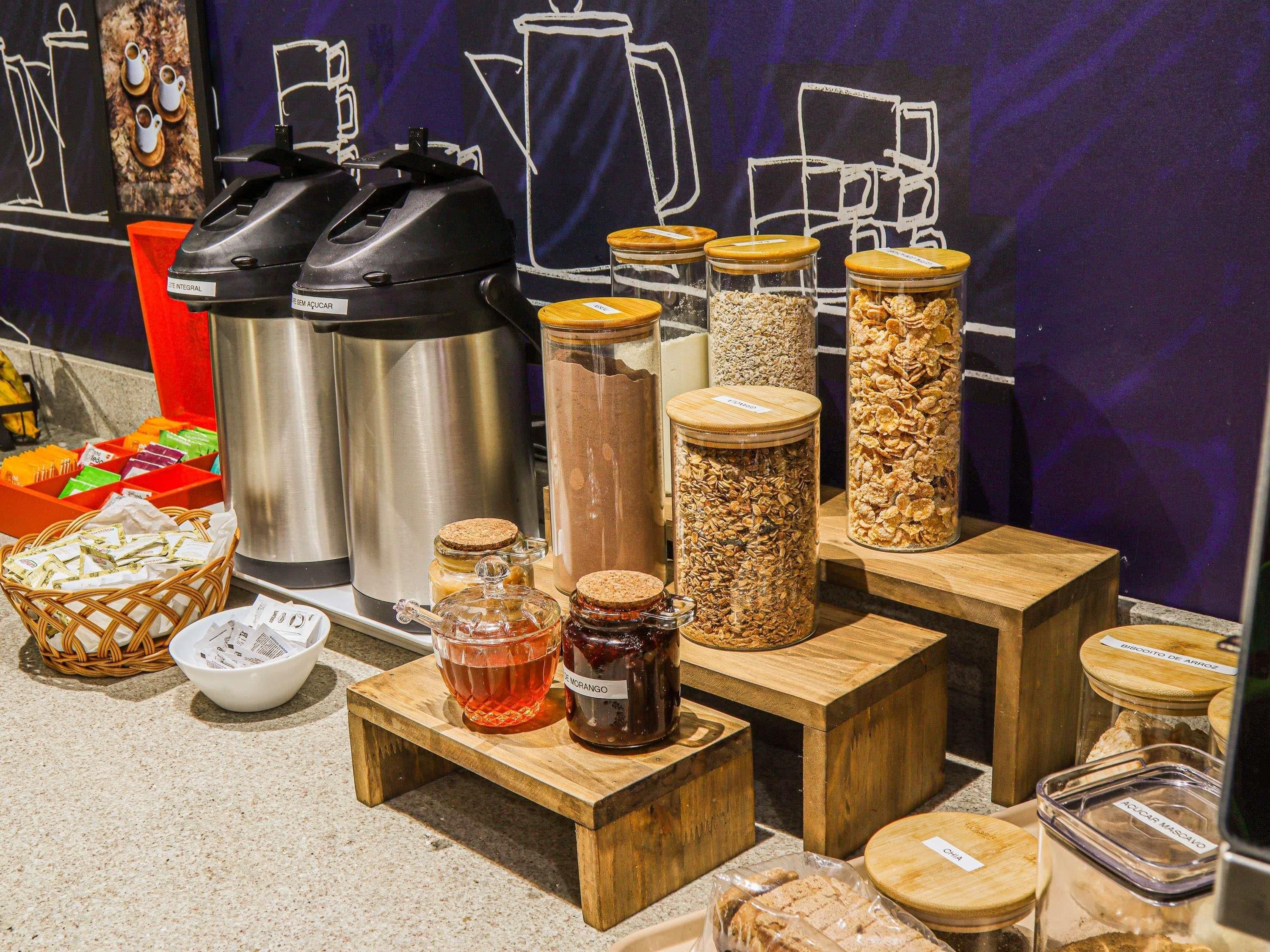 Diversos alimentos y condimentos expuestos sobre mesas y estantes de madera, con una cafetera y un hervidor de agua al fondo.