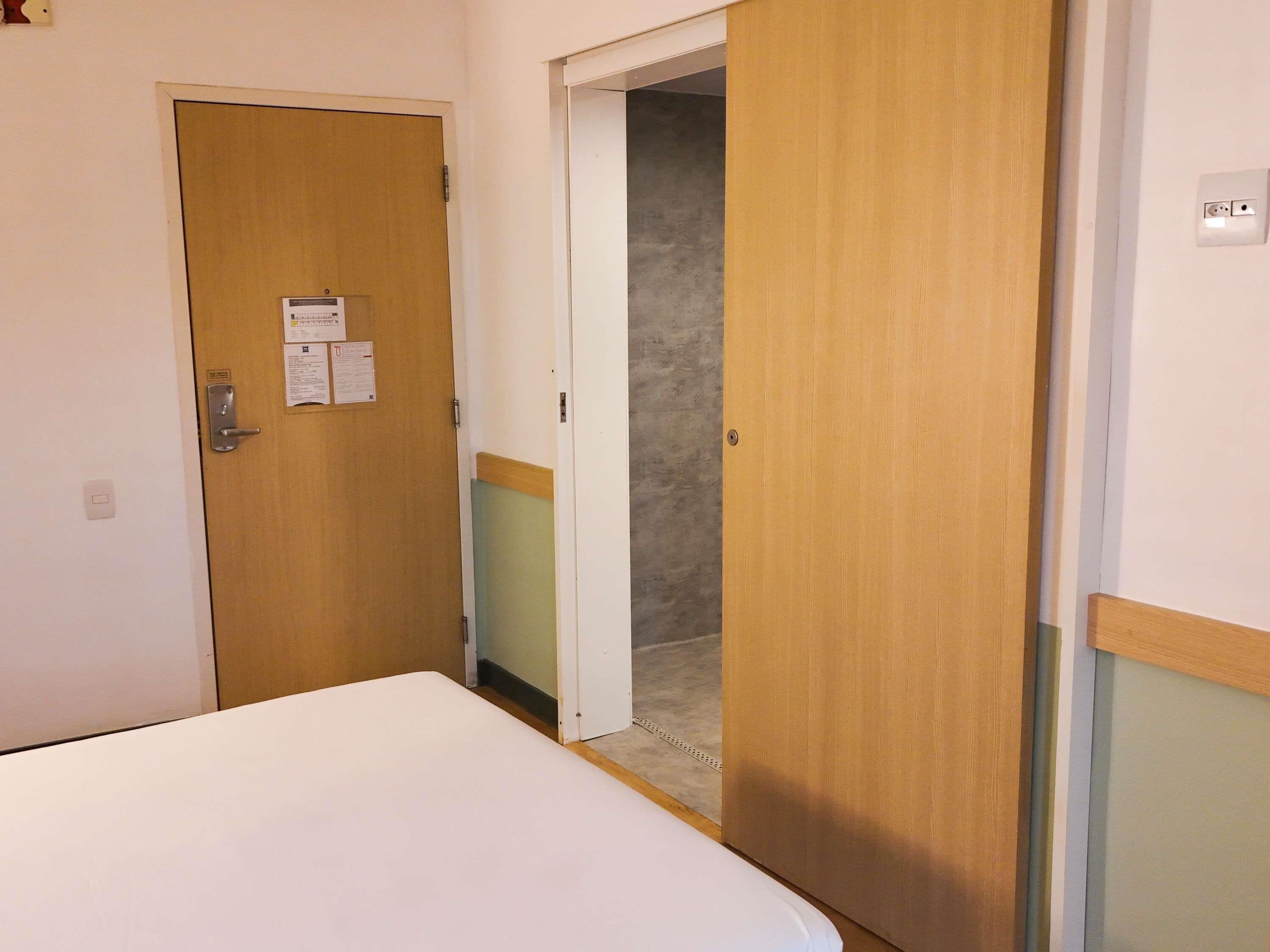 A hotel room with a bed, a wooden door, and a small closet.