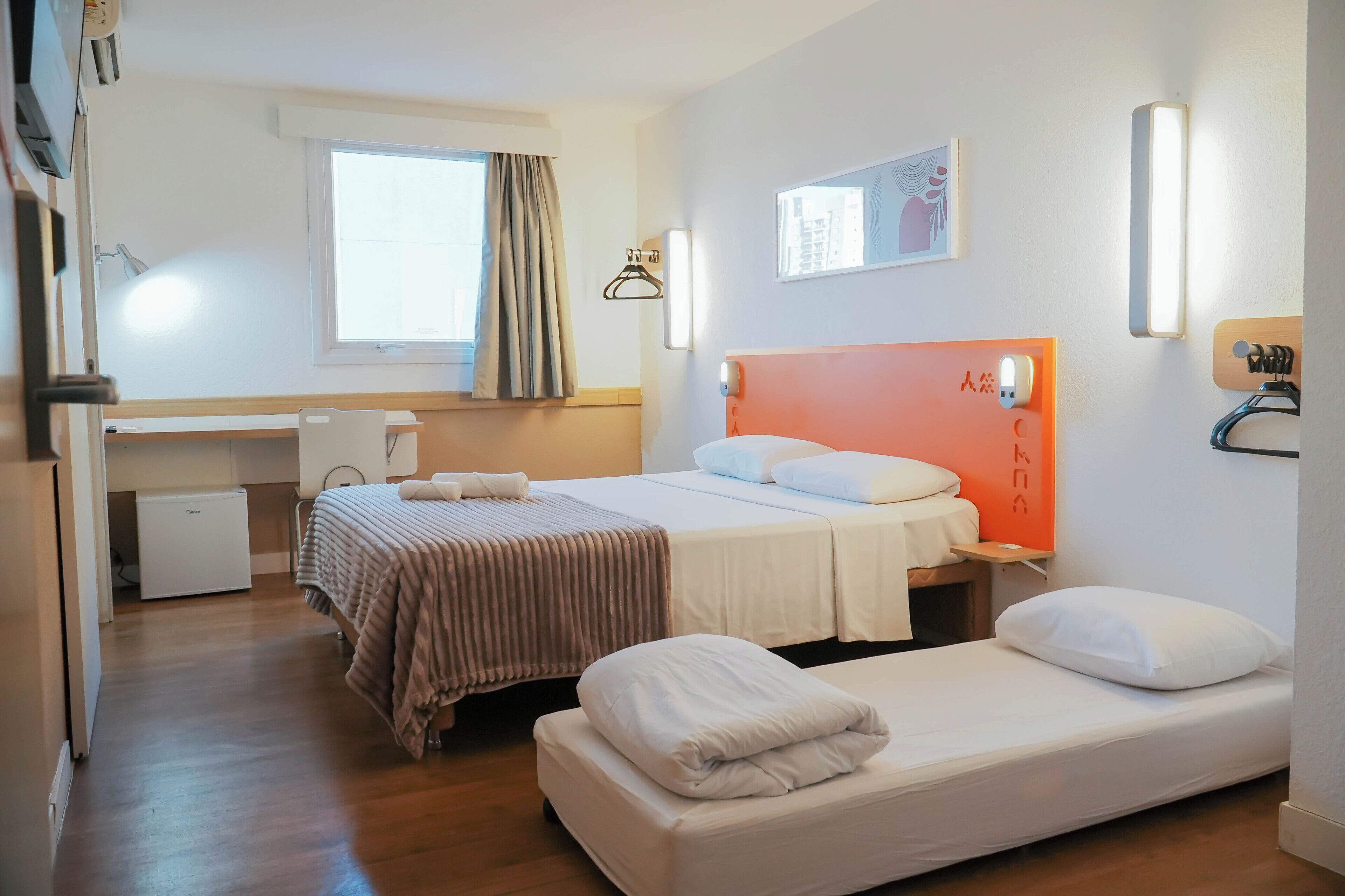 Ein Hotelzimmer mit zwei Betten, einem Schreibtisch und einem Vorhangfenster.