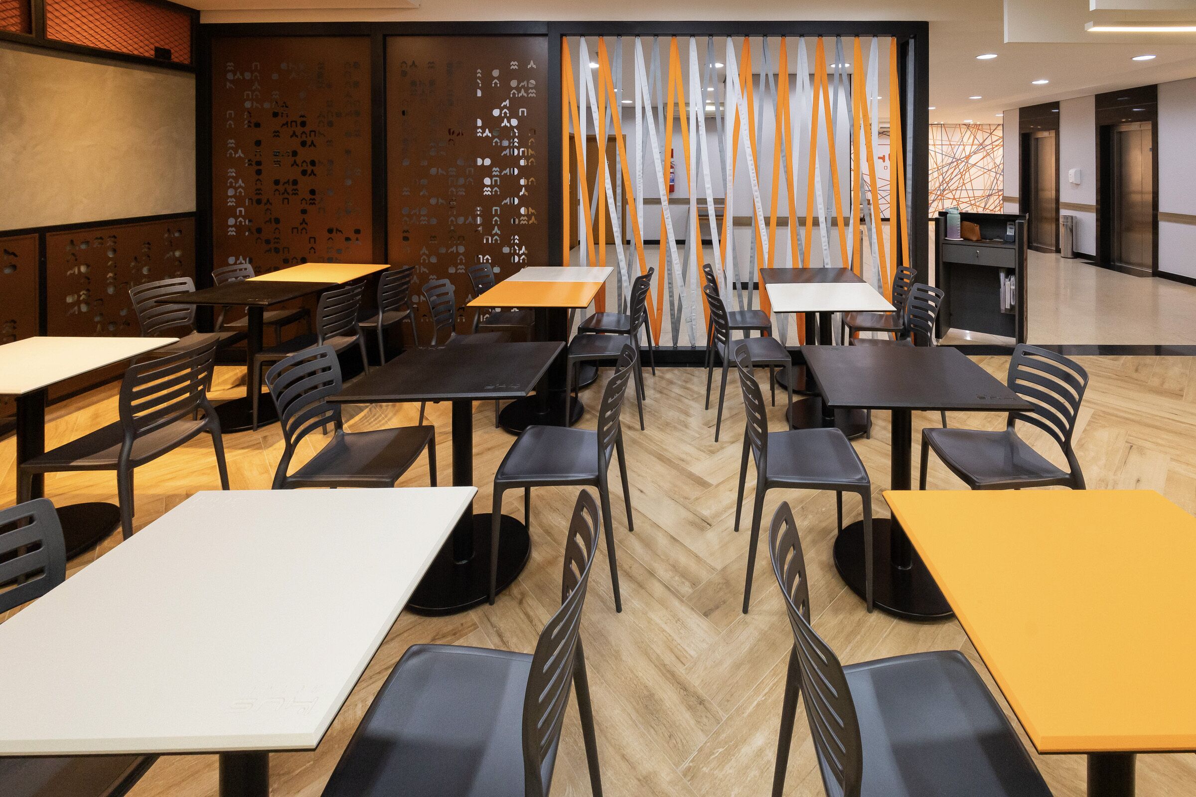 A modern restaurant with multiple tables and chairs, a wooden floor, and a decorative wall with vertical elements.