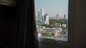 Blick aus einem Fenster auf eine Stadtansicht mit hohen Gebäuden, einer Straße und etwas Grün.