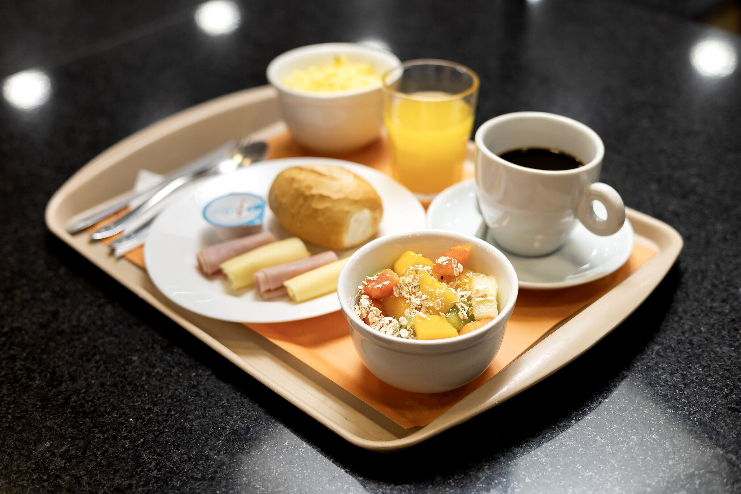 A breakfast tray with a plate of food, a bowl of fruit, a glass of orange juice, and a cup of coffee.