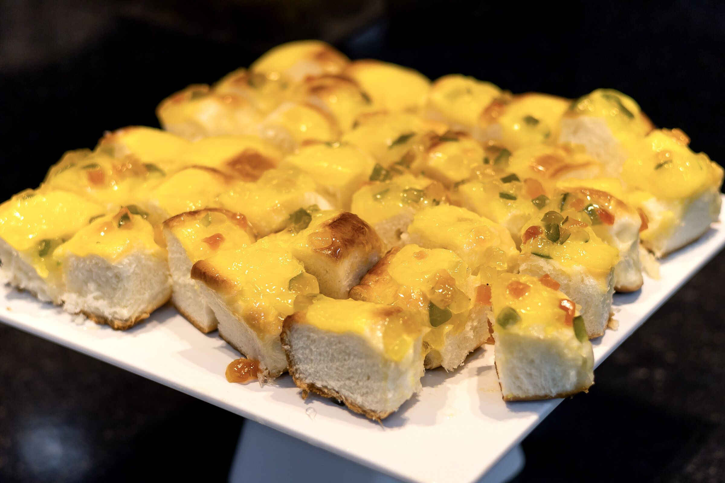 Prato branco retangular com vários pedaços de pão cobertos por queijo derretido e ervas verdes.
