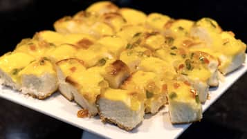 Prato branco retangular com vários pedaços de pão cobertos por queijo derretido e ervas verdes.