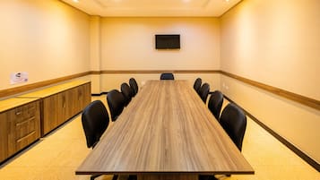 Una sala de conferencias con una larga mesa, sillas negras, un televisor en la pared y armarios de madera.