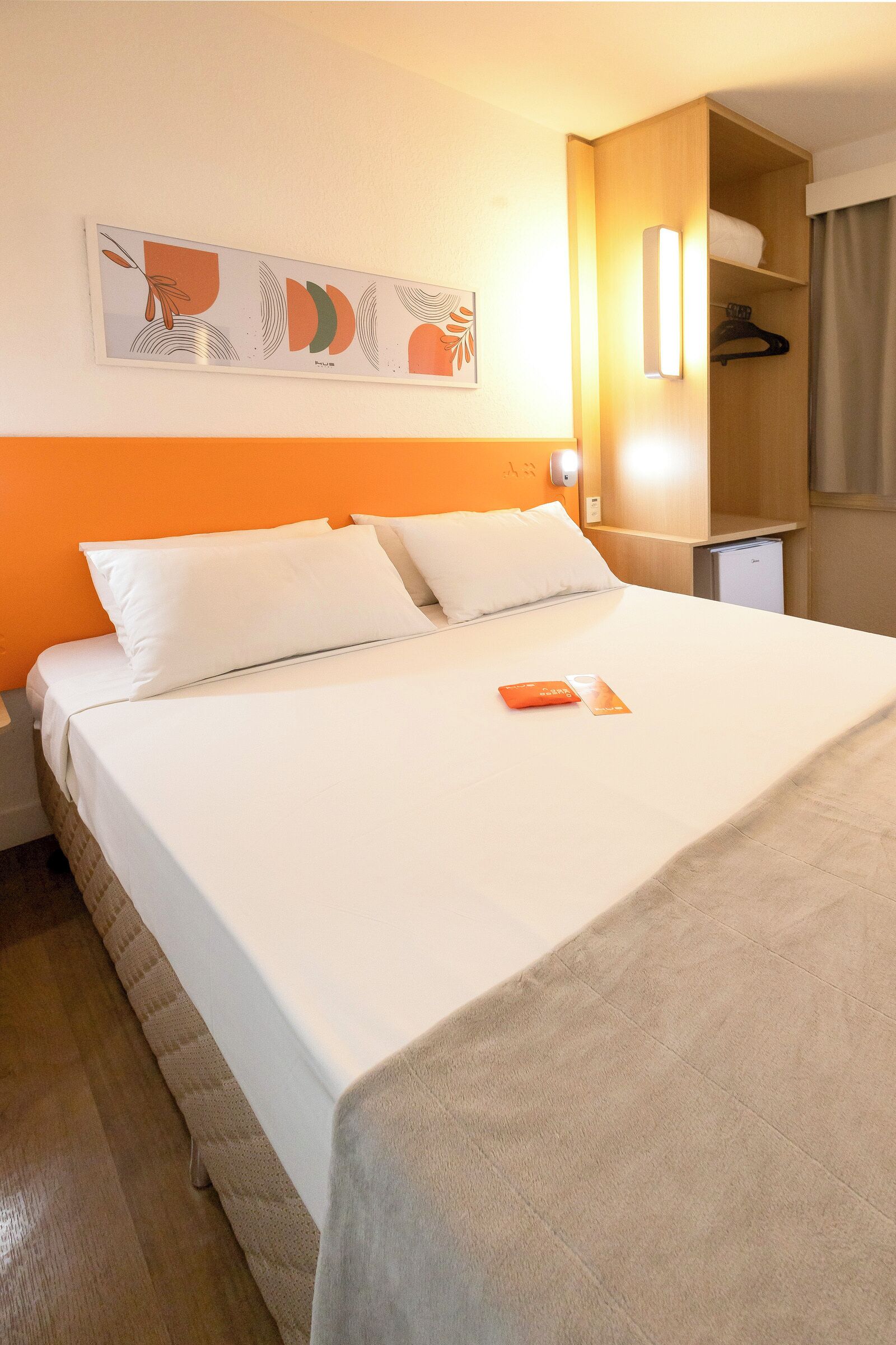 A neatly made bed with white linens and a single orange booklet on it.