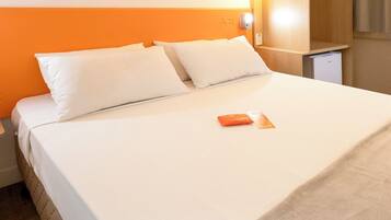 A neatly made bed with white linens and a single orange booklet on it.