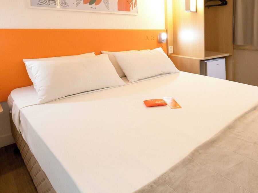 A neatly made bed with white linens and a single orange booklet on it.