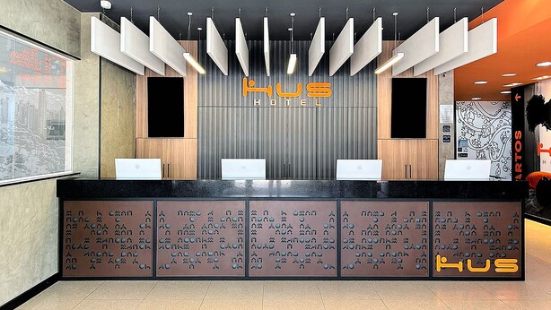 Ein Hotelrezeptionstresen mit modernem Design, der ein zentrales Logo und mehrere Schalter umfasst.
