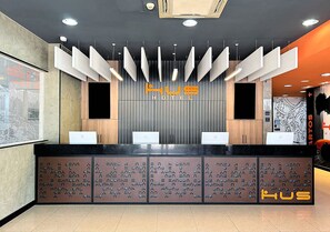 A hotel reception desk with a modern design, featuring a central logo and multiple counters. - HUS HOTEL MARINGA (Maringá)