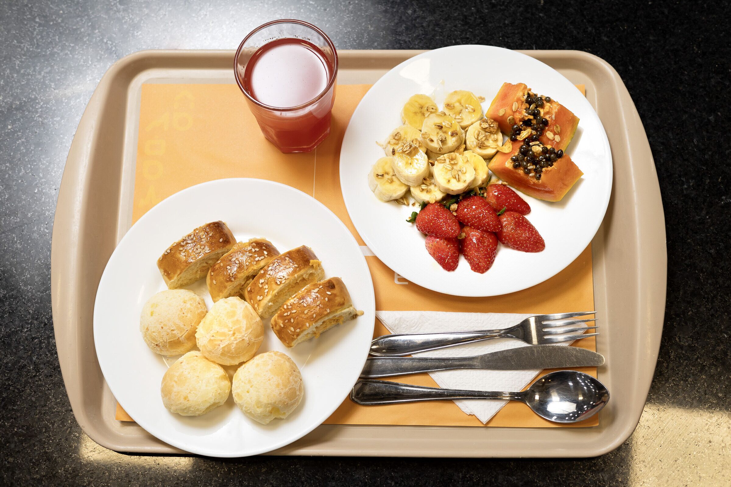 Un plateau avec deux assiettes de nourriture, un verre de jus de fruits et des couverts.