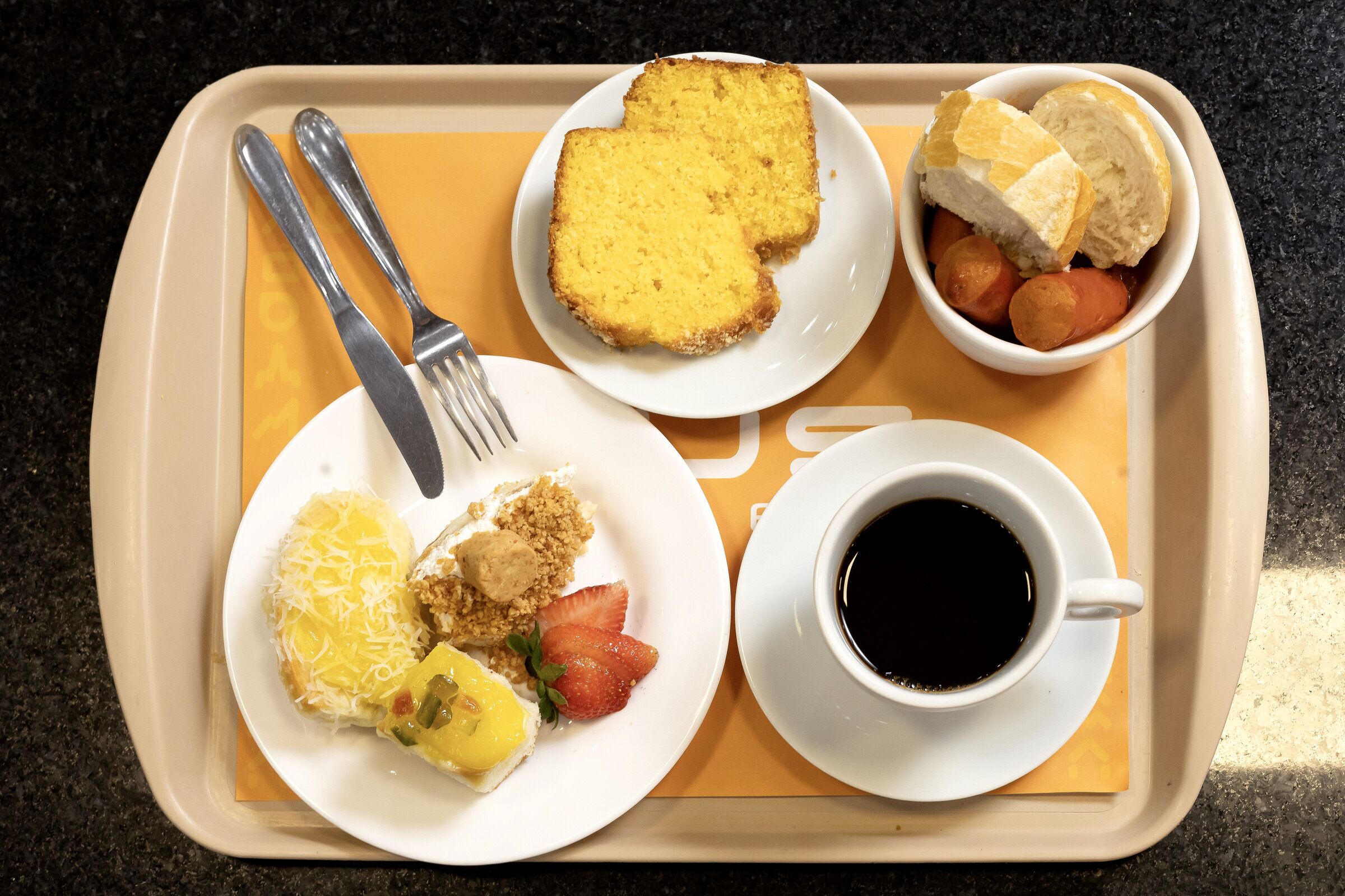 Una bandeja con alimentos para el desayuno, como tostadas, salchichas, fresas y una taza de café.