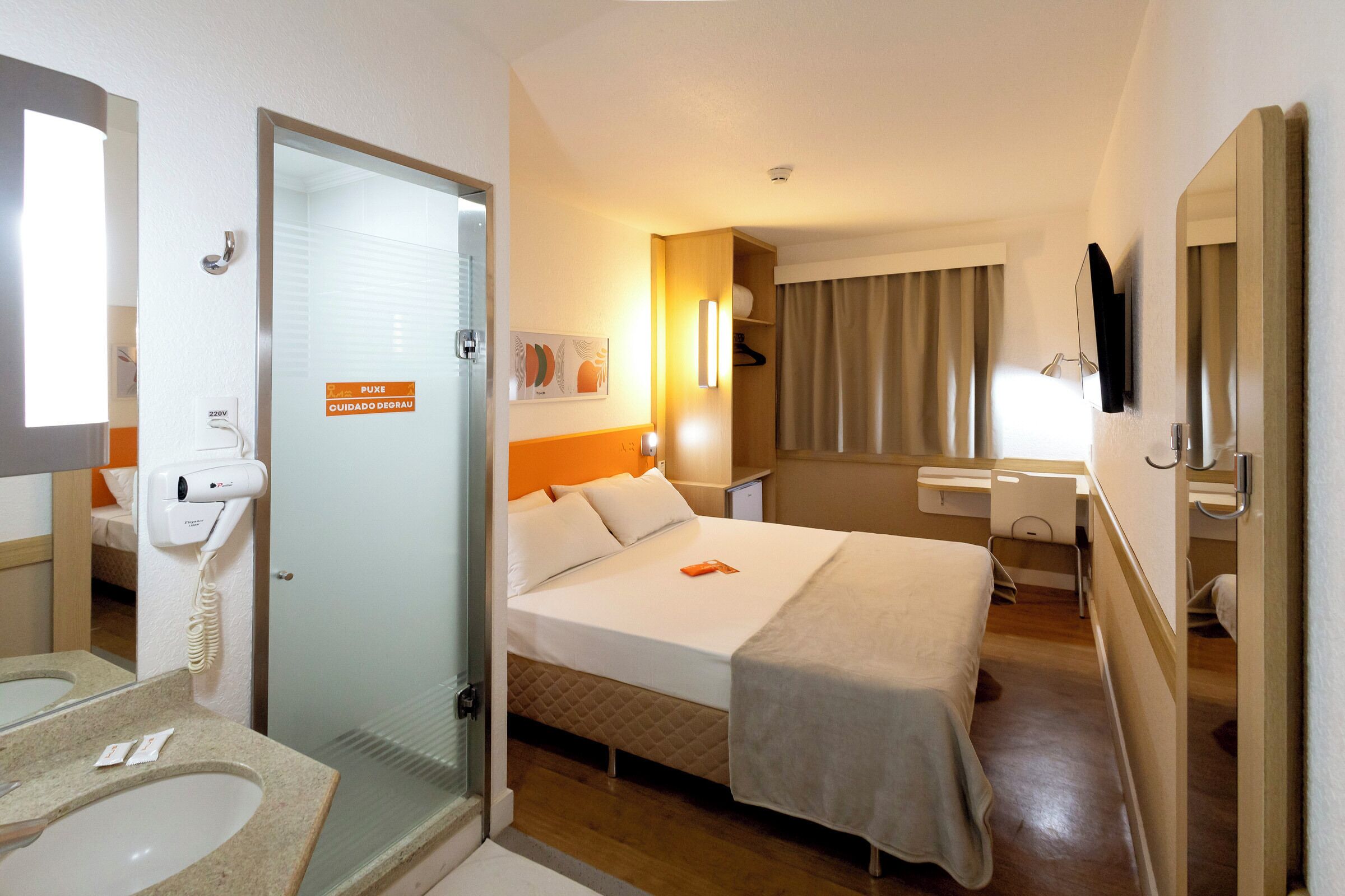 A hotel room with a bed, a bathroom with a sink and mirror, and a door leading to another room.