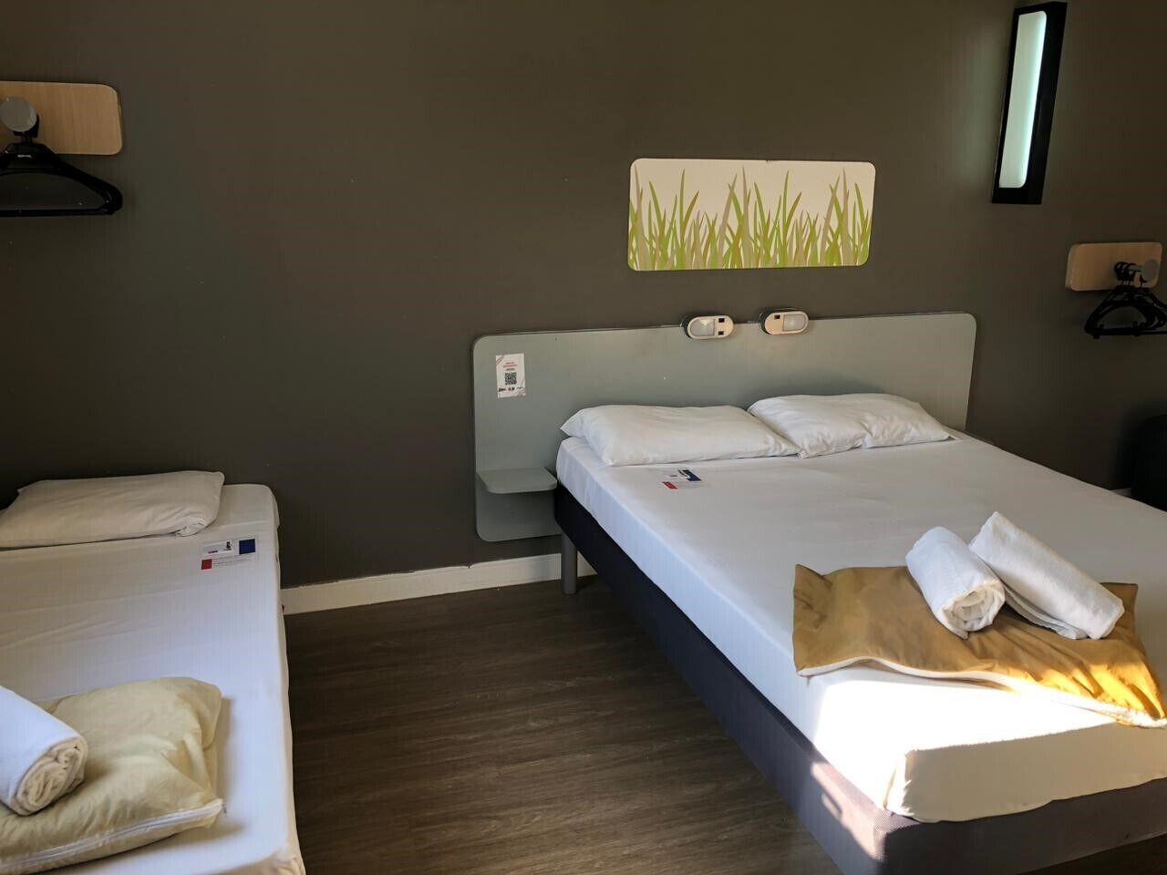 Una habitación de hotel con dos camas, un cabecero, una lámpara de pared y una obra de arte en la pared.