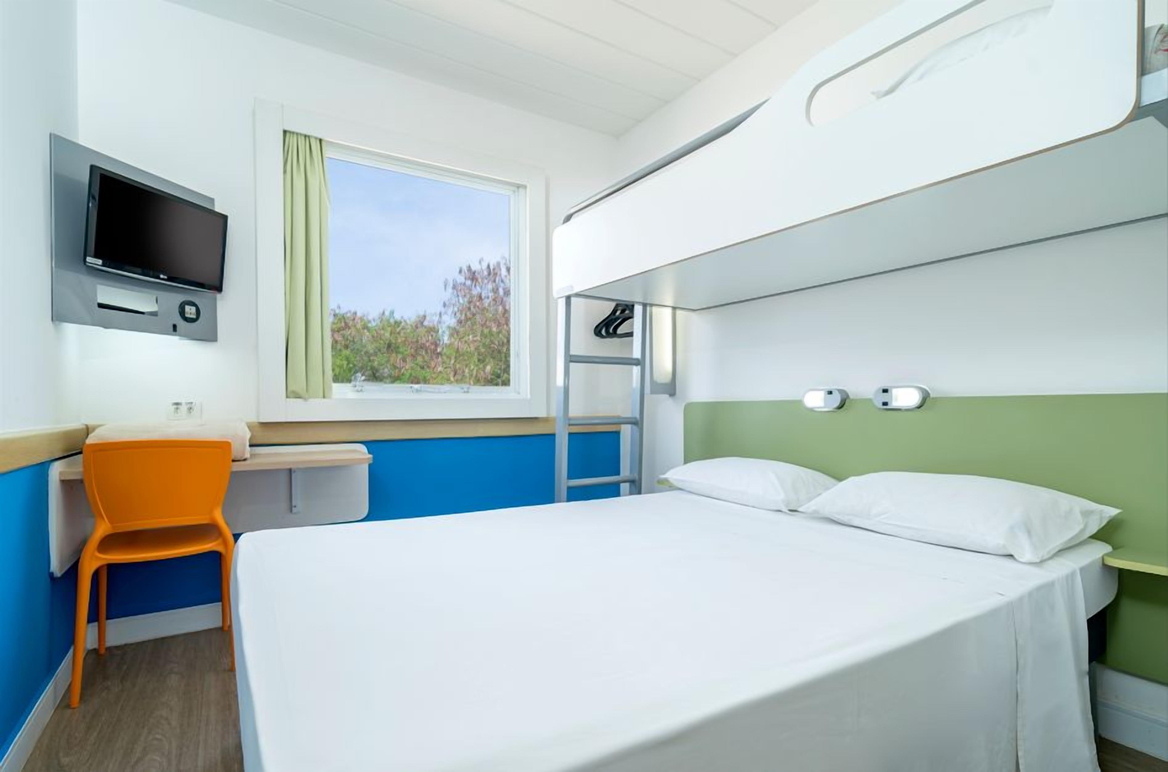 Een hotelkamer met een bed, een bureau, een stoel, een televisie en een raam met uitzicht.