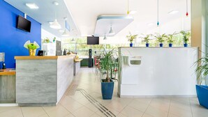 A modern reception area with a blue wall, a reception desk, a TV, and potted plants. - ibis budget Piracicaba (Piracicaba)