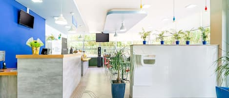 A modern reception area with a blue wall, a reception desk, a TV, and potted plants.