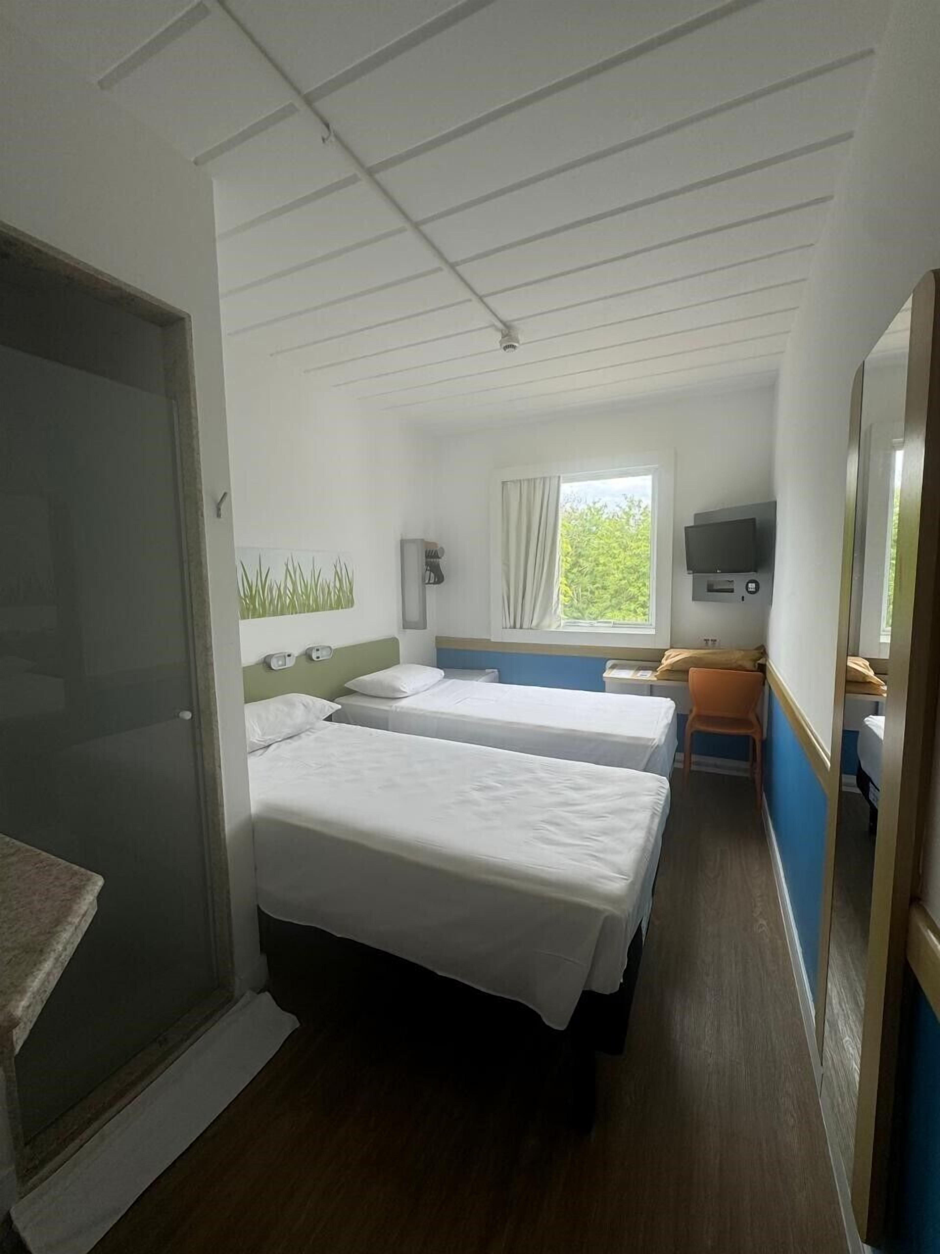 Una habitación de hotel con dos camas, televisión, ventana con cortinas y una mesita.