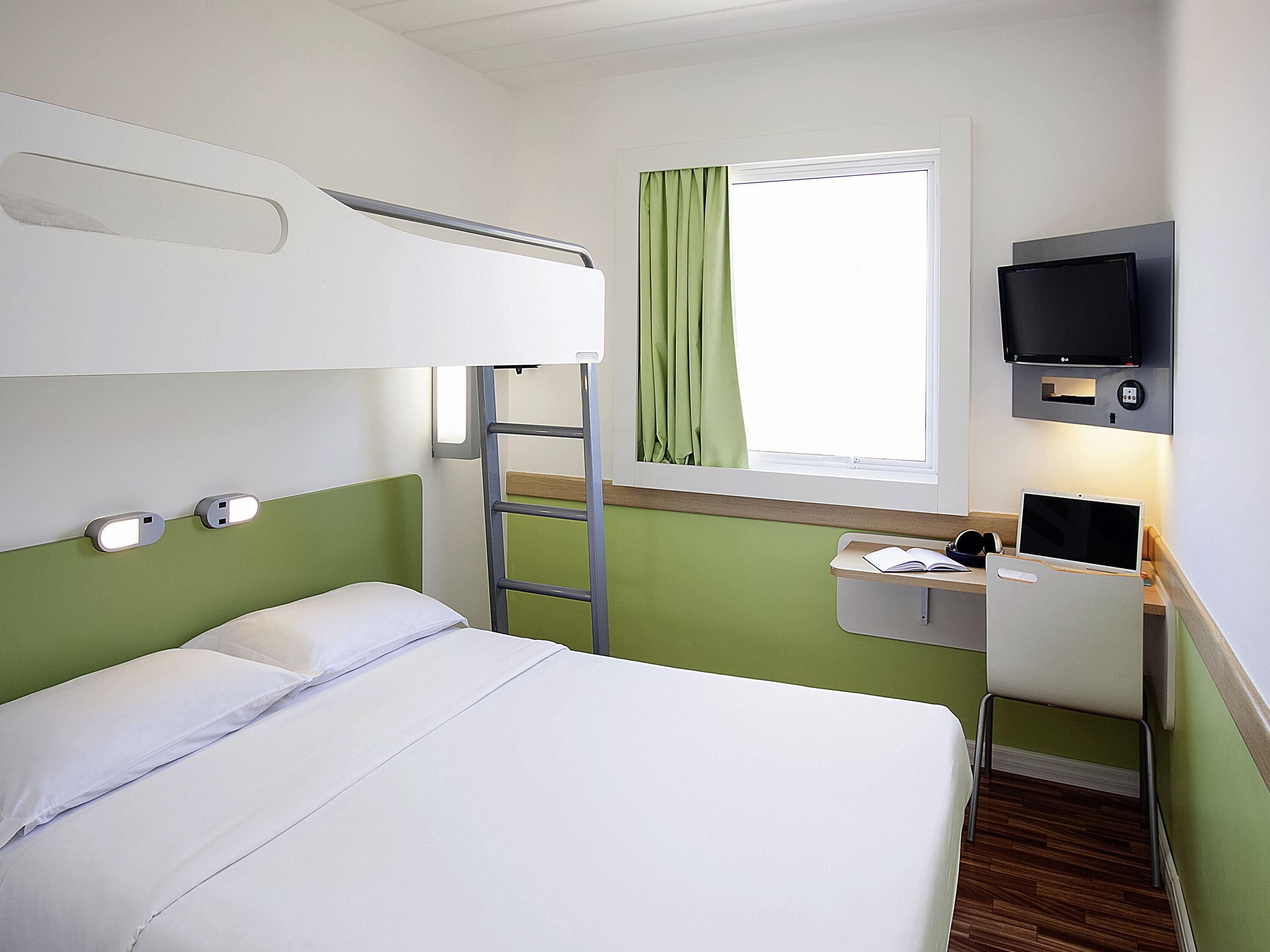 Una cama litera con escalera, un escritorio con computadora y un televisor en una habitación con paredes verdes.