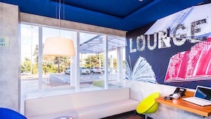 A modern lounge area with a large window, a sofa, a wooden table with a laptop, and a colorful mural on the wall.