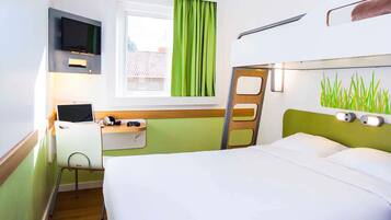 Quarto de hotel com cama, escrivaninha com laptop, televisão e janela com cortinas.