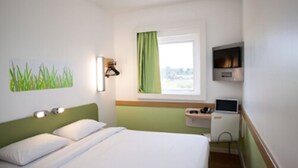 Ein Hotelzimmer mit einem Bett, einem Schreibtisch mit Computer, einem Fernseher und einem Fenster mit Blick.
