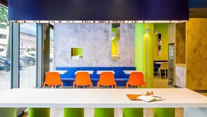 Un'area salotto moderna con un tavolo bianco, sedie blu e arancioni, e dettagli in verde e giallo.