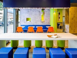 Un área de descanso moderna con una mesa blanca, sillas azules y anaranjadas, y detalles en verde y amarillo.