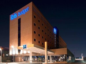 Un hotel de diseño moderno, con un llamativo letrero de 'ibis budget', múltiples ventanas y un área de acceso cubierta.