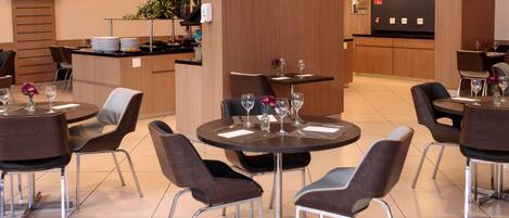 Interior de un restaurante moderno con mesas redondas, sillas y una zona de cocina identificada como 'Ibis kitchen'.