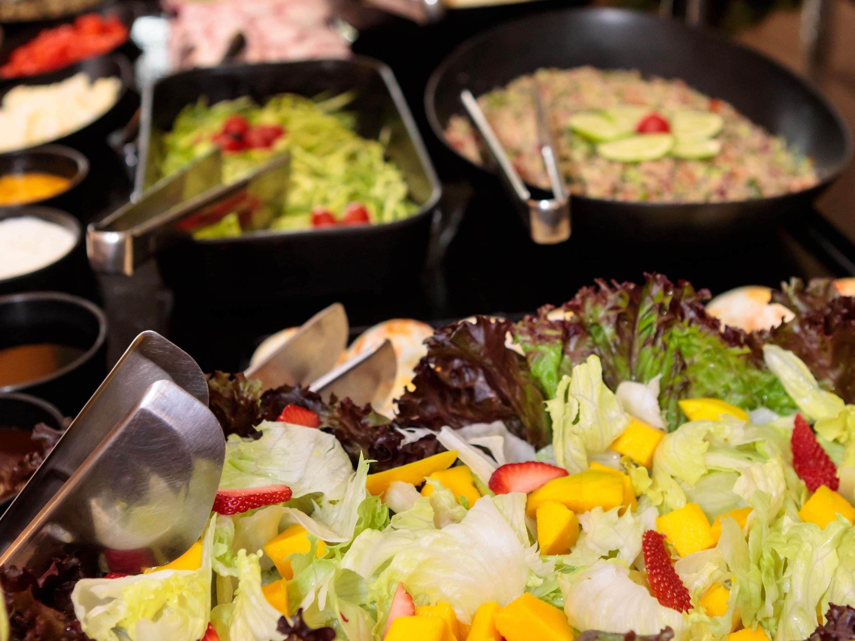 A buffet with various dishes including a salad with strawberries and mango.