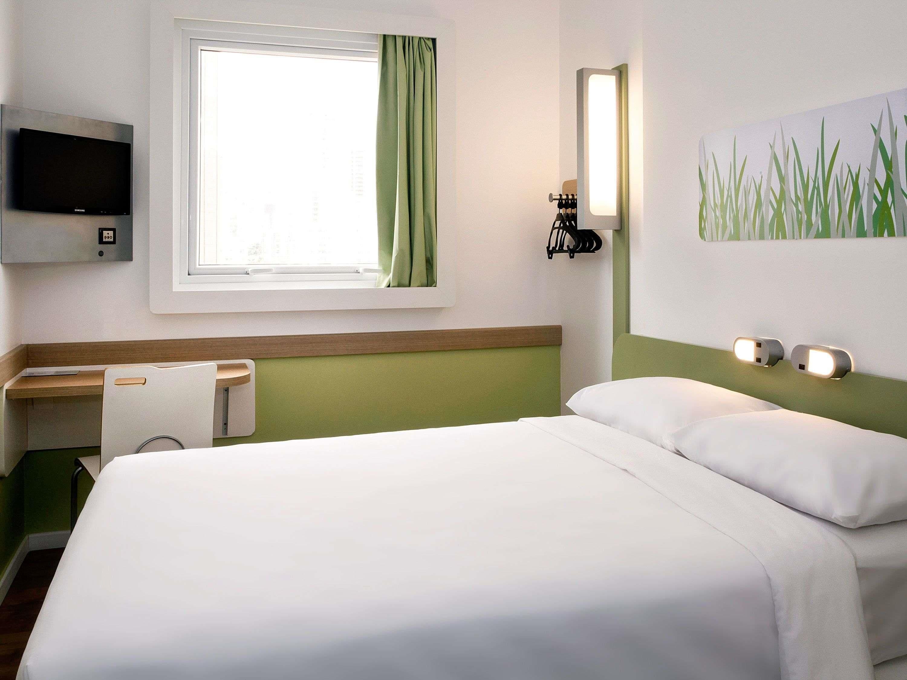 Une chambre d’hôtel avec un lit, un bureau, une télévision et un tableau au mur.