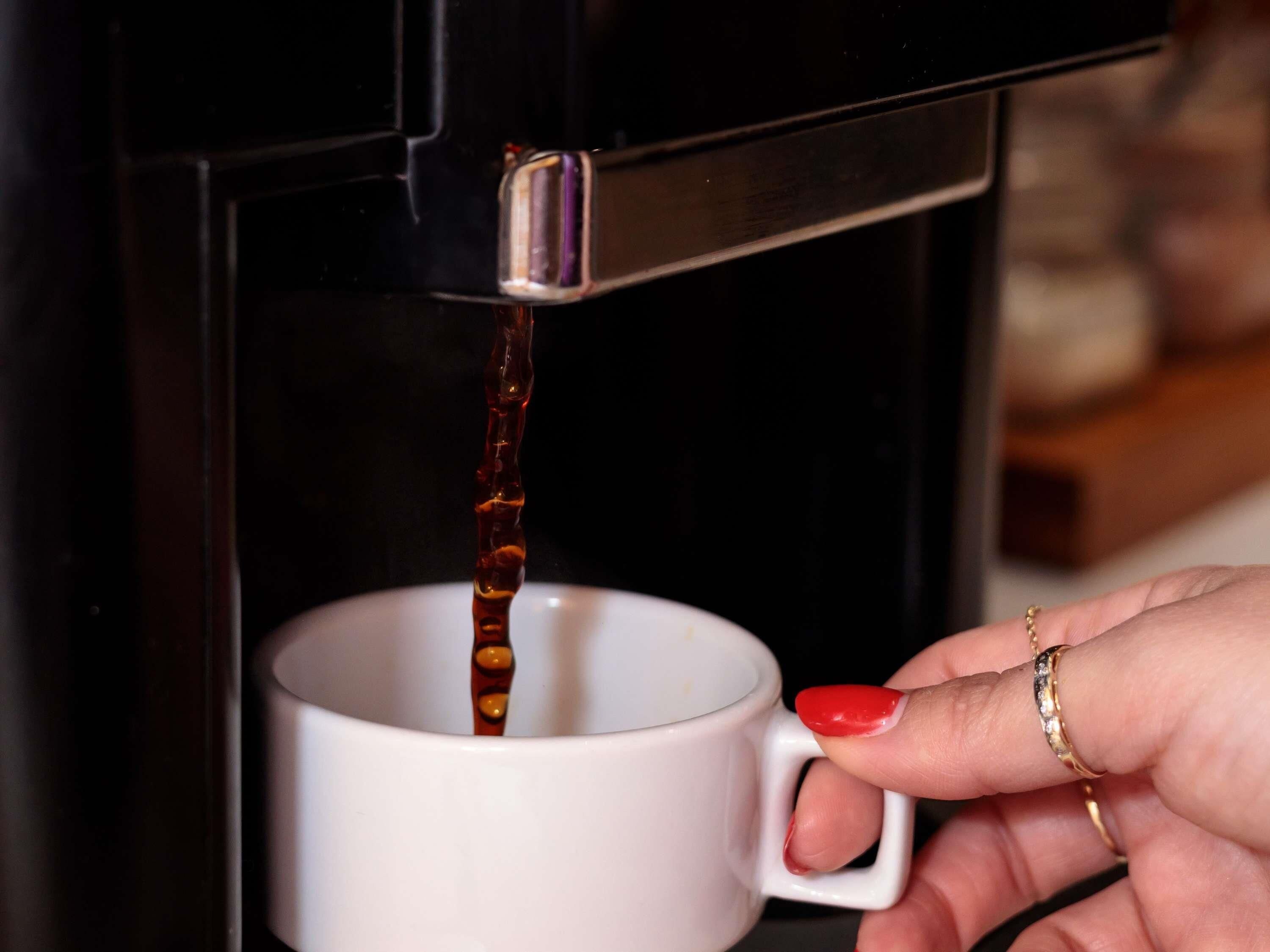A hand holding a white mug under a coffee machine.