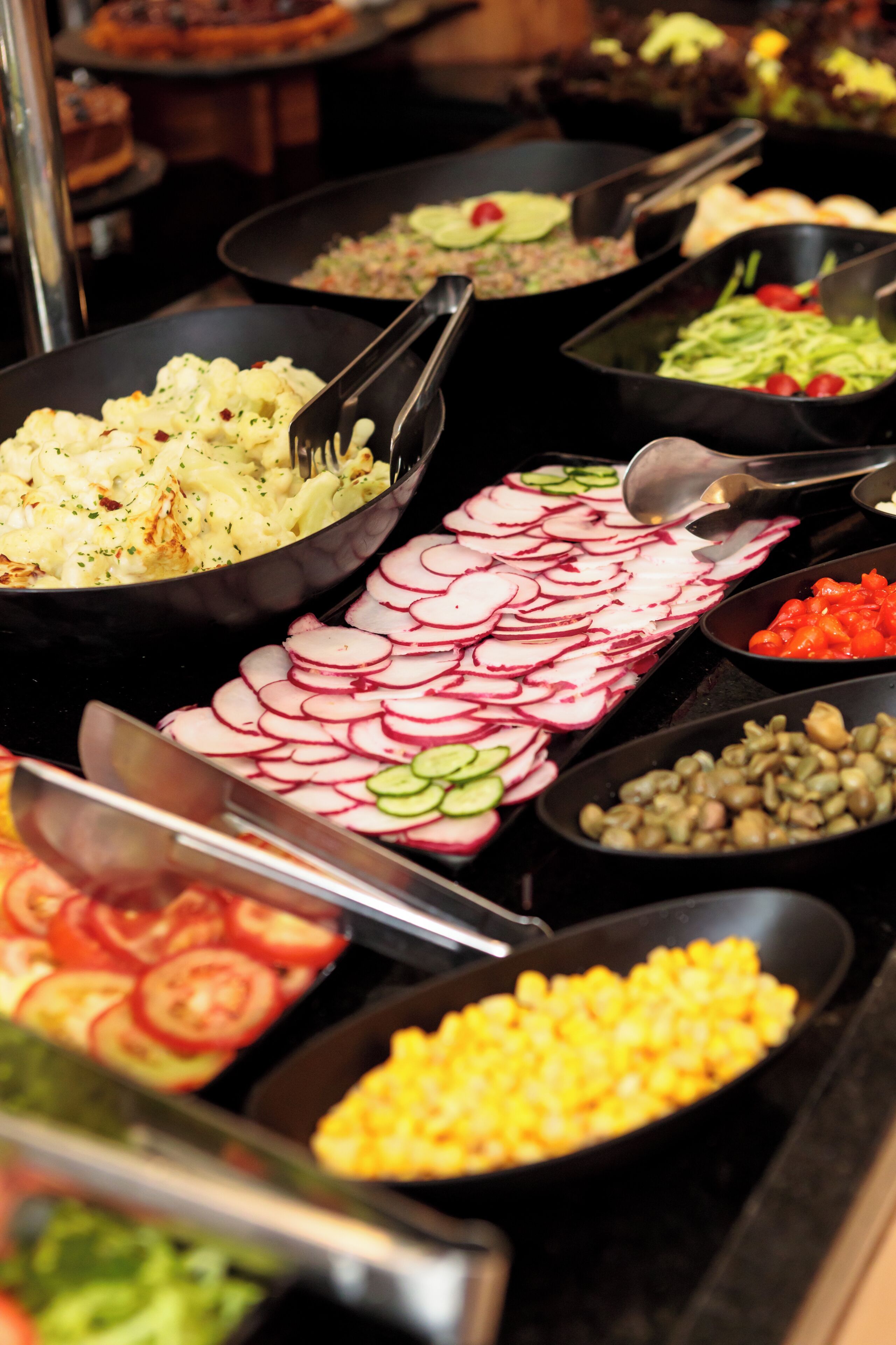 A buffet with various food items including sliced radishes, cucumbers, tomatoes, and corn.