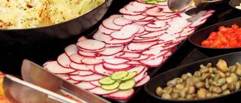 Un buffet proposant une variété d’aliments, notamment des radis en tranches, des concombres, des tomates et du maïs.