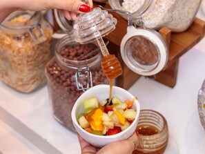 A person holding a bowl of fruit salad with honey being drizzled over it. - ibis budget BH Afonso Pena Savassi (Belo Horizonte)