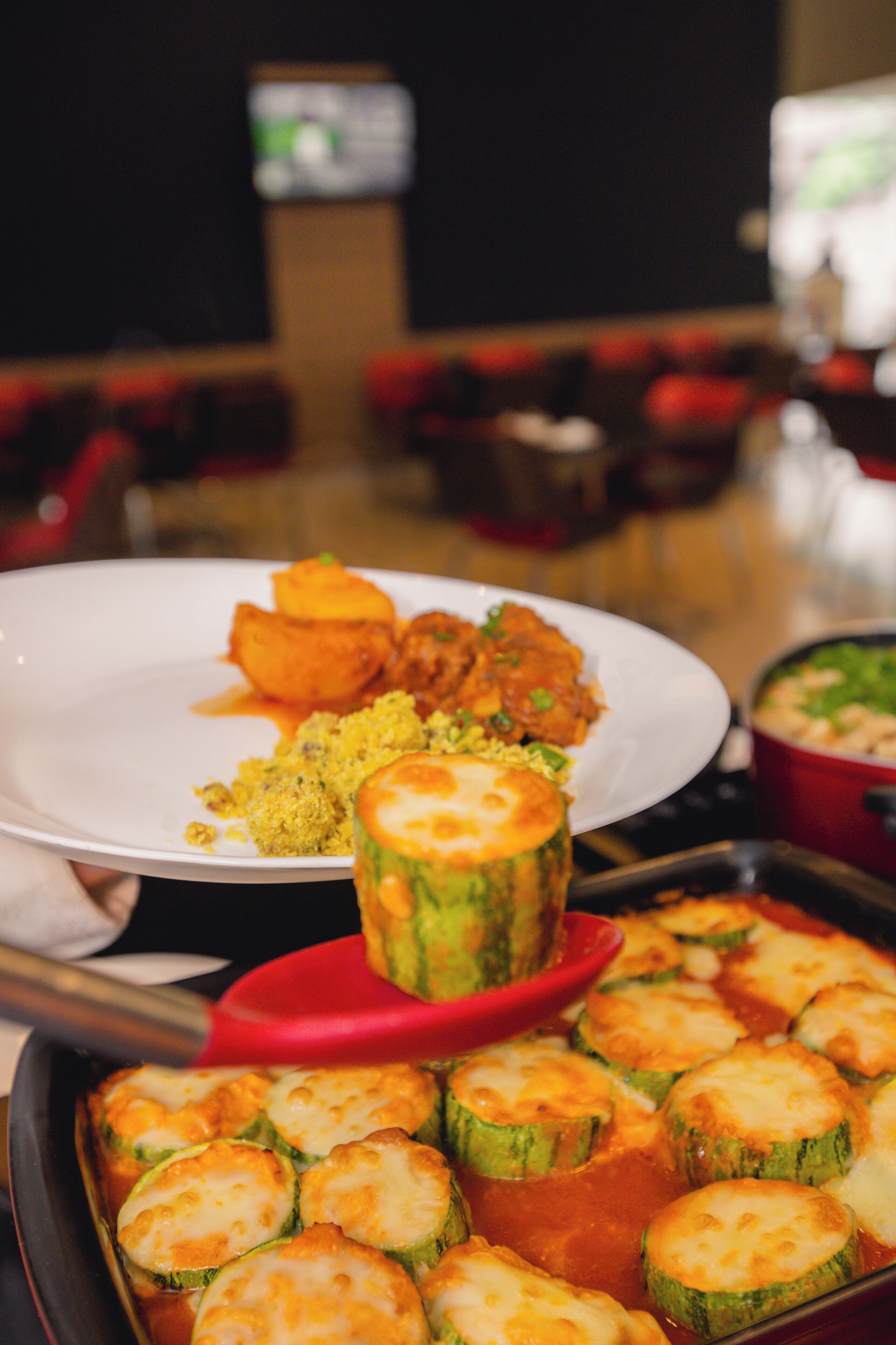 Uma mesa de jantar com diversos pratos, incluindo um prato com molho vermelho, uma tigela de arroz amarelo e uma travessa com fatias de abobrinha assada.