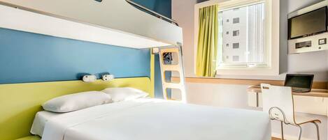 A hotel room with a bunk bed, a desk with a laptop, a television, and a window with curtains.