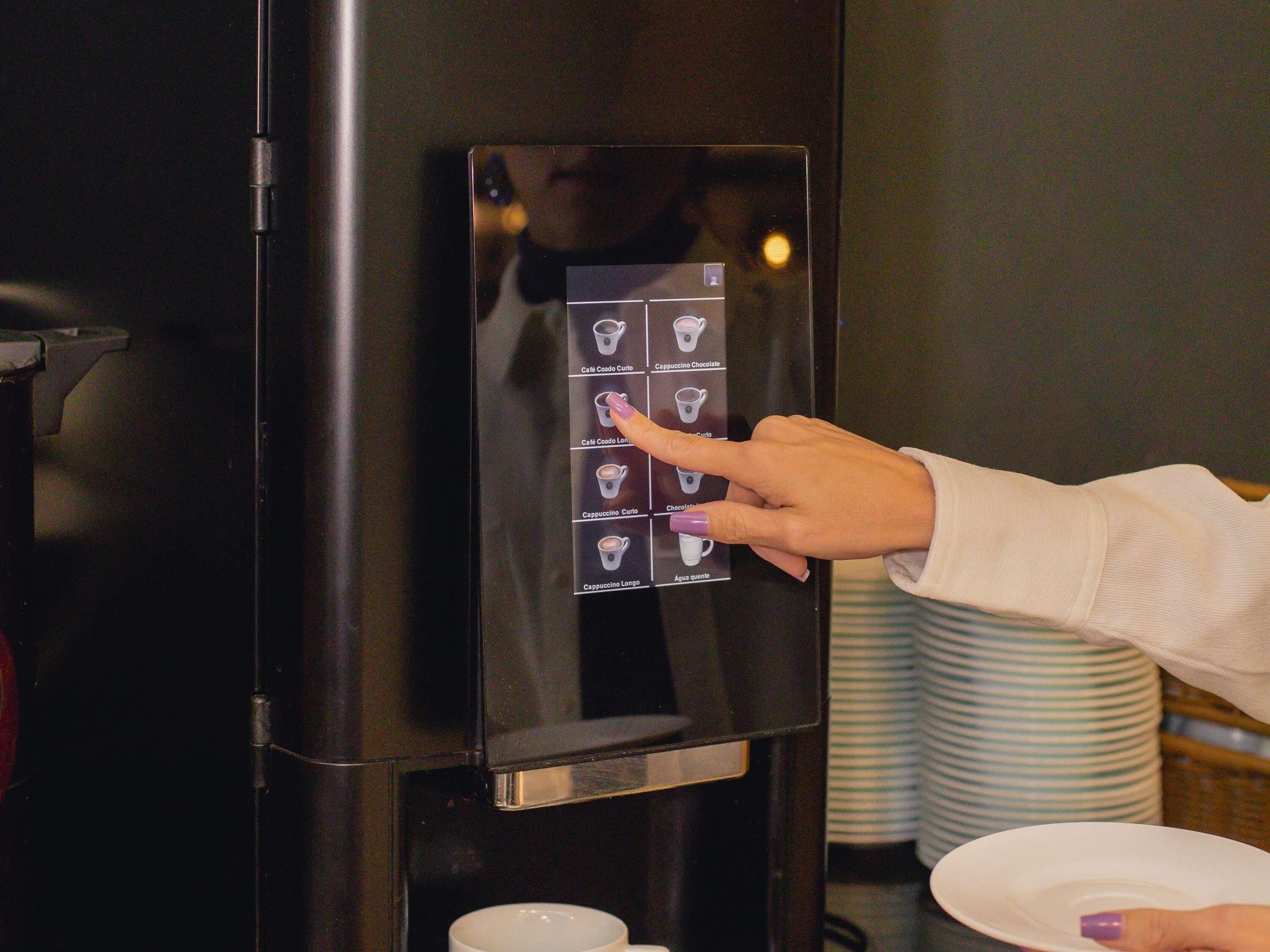 Una persona utilitzant una màquina de cafè amb pantalla tàctil i diverses opcions de begudes.