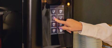 A person using a touchscreen coffee machine with various drink options.