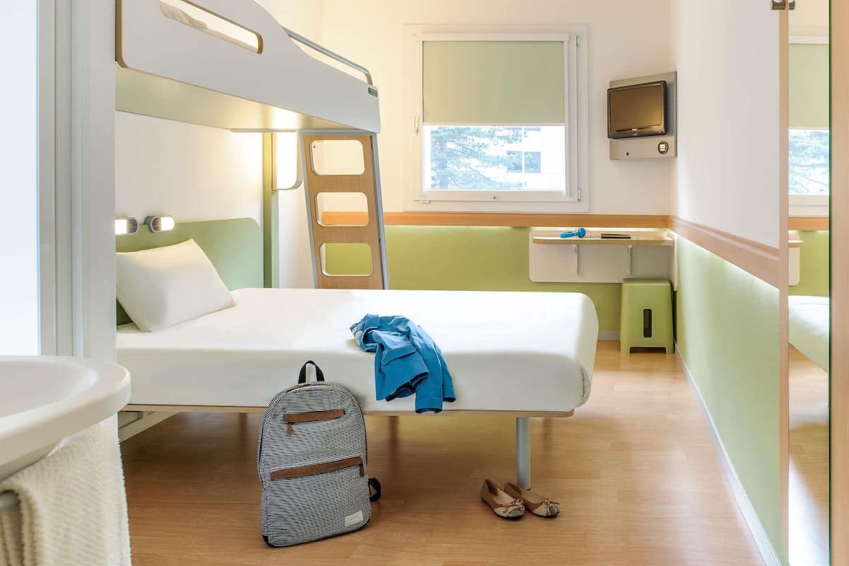 A compact room with bunk beds, a small desk, a TV, and a window with a view.