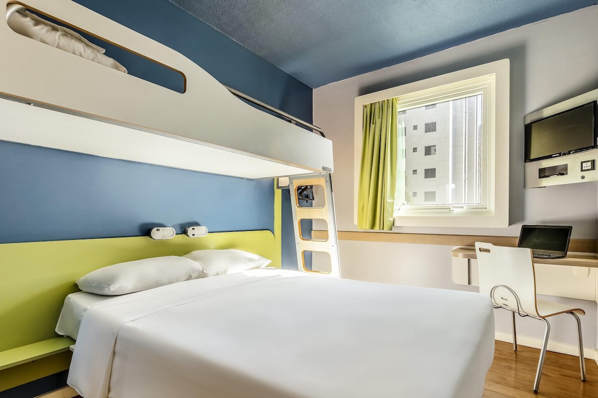A hotel room with a bed, a desk, a chair, a TV, and a window with curtains.