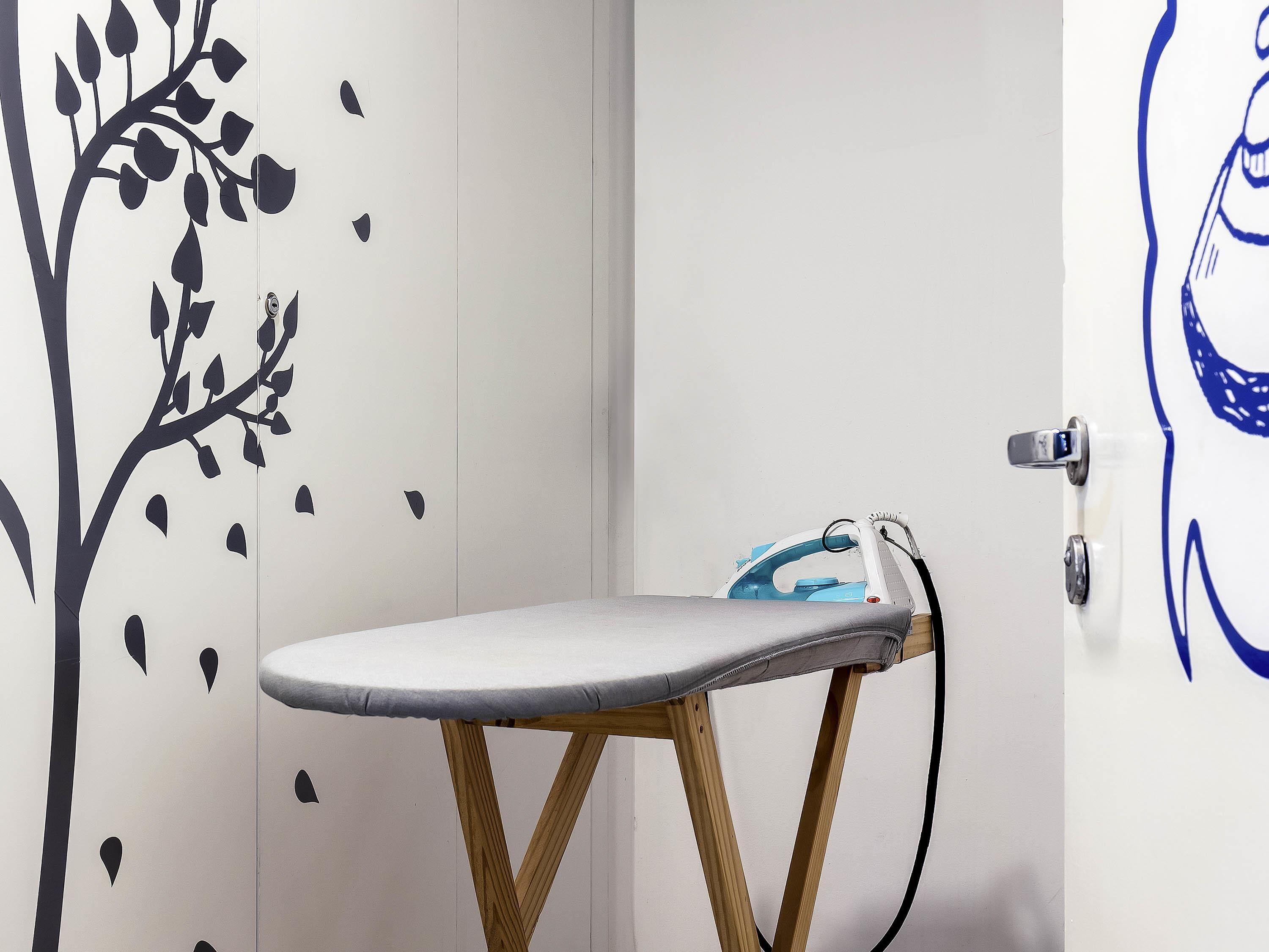 A room with a wooden ironing board, a wall with a tree decal, and a door with a blue design.
