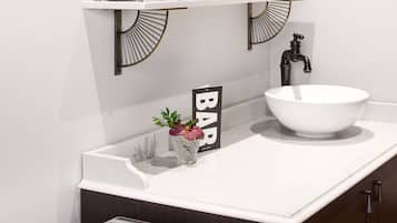 A modern bathroom with a white sink, a glass bowl sink, and a shelf with toiletries.