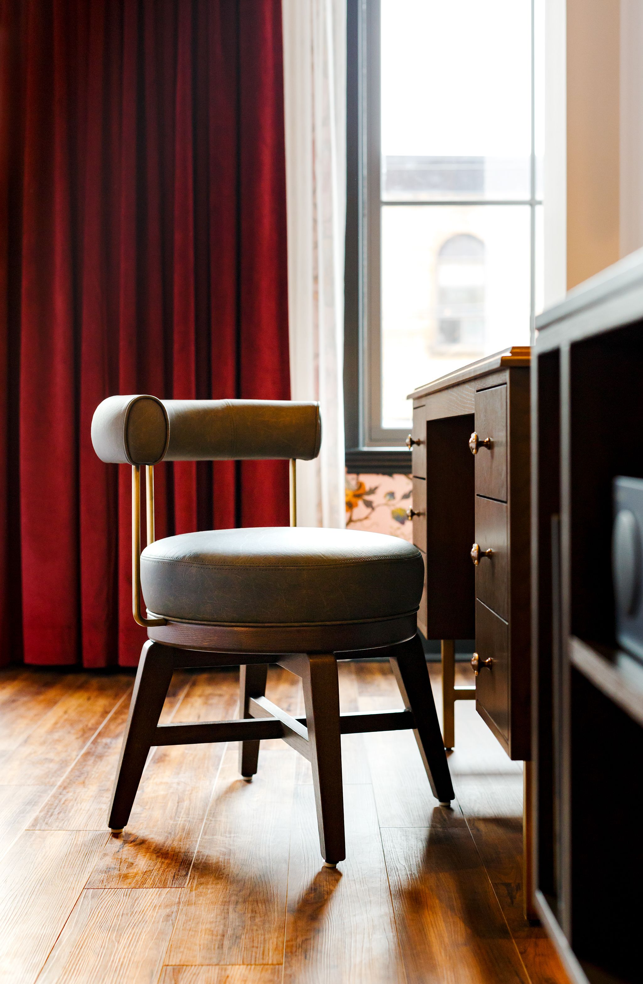 A modern chair with a cushioned seat and a metal frame, positioned in front of a wooden cabinet and a window with red curtains.