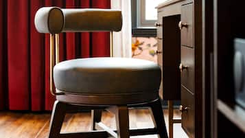 A modern chair with a cushioned seat and a metal frame, positioned in front of a wooden cabinet and a window with red curtains.