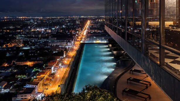 Un hotel di grattacielo con piscina sul tetto che si affaccia su una città illuminata di notte.