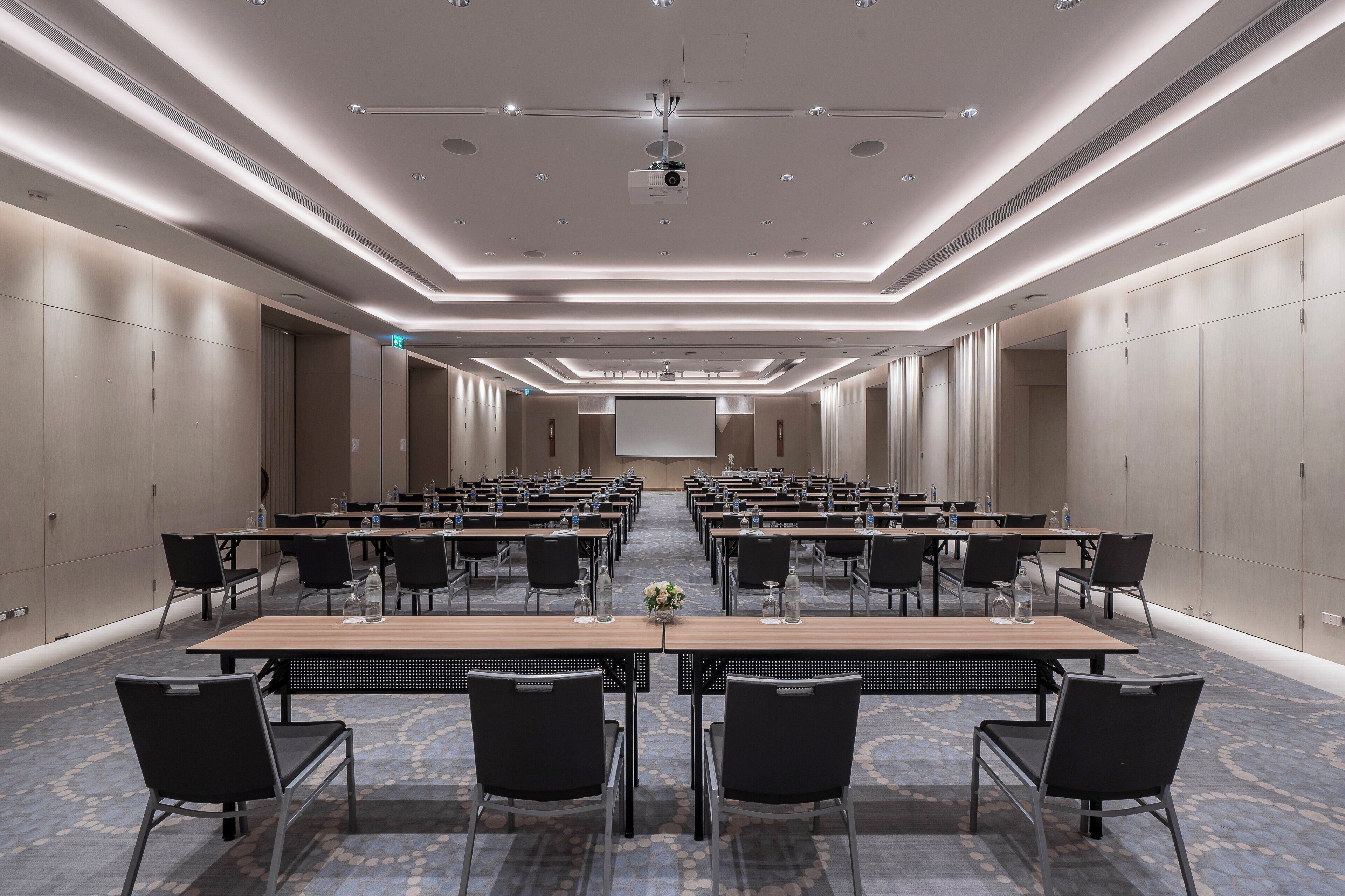 A conference room with rows of tables and chairs, equipped with water bottles and glassware.